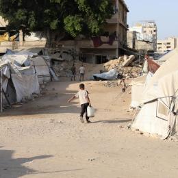 Un petit garçon peine sous le poids d'un jerrican d'eau qu'il doit ramener jusqu'à la tente où vit sa famille déplacée, territoires palestiniens occupés, octobre 2025.