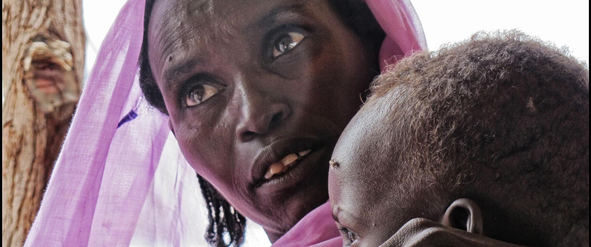 Une femme tient son enfant dans les bras, en attendant de recevoir des soins médicaux dans un centre de santé MSF au Nord-Darfour. Soudan. 2014